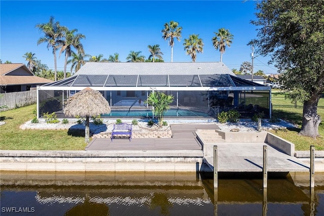 rear view of house featuring a lanai, a water view, and a lawn