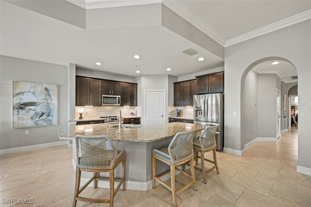 kitchen featuring light stone counters, stainless steel appliances, a center island with sink, a breakfast bar area, and dark brown cabinetry