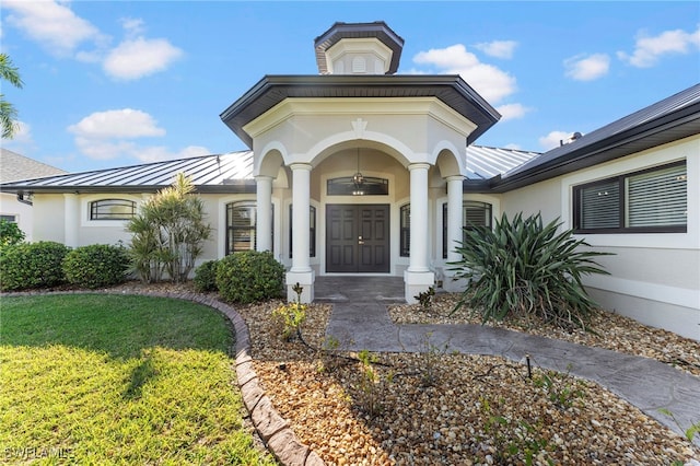 property entrance featuring metal roof, a standing seam roof, a lawn, and stucco siding