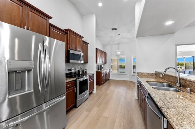 kitchen with light stone counters, stainless steel appliances, lofted ceiling, a sink, and light wood-type flooring