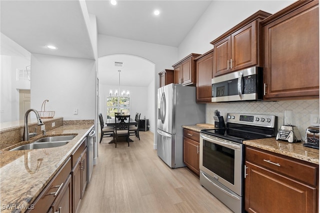 kitchen featuring light wood-style flooring, stainless steel appliances, a sink, light stone countertops, and tasteful backsplash