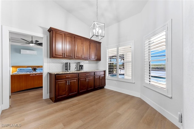 kitchen featuring lofted ceiling, decorative backsplash, light wood-style floors, an AC wall unit, and light stone countertops