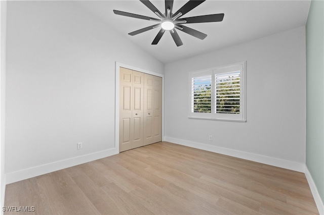 unfurnished bedroom featuring lofted ceiling, a closet, light wood-type flooring, and baseboards