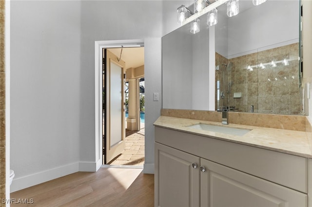 full bathroom with tiled shower, vanity, baseboards, and wood finished floors