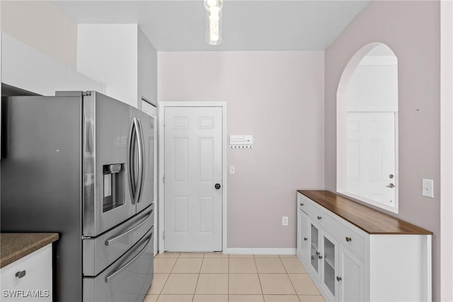 kitchen with stainless steel refrigerator with ice dispenser, light tile patterned flooring, and white cabinetry