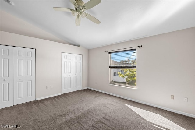 unfurnished bedroom featuring ceiling fan, vaulted ceiling, two closets, and dark carpet