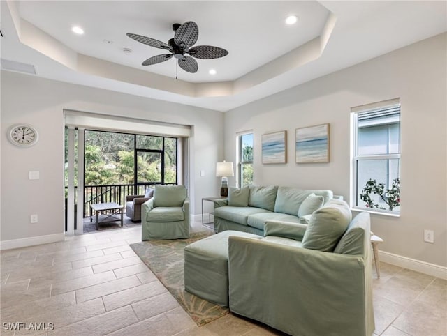 living room with a tray ceiling, a wealth of natural light, and ceiling fan