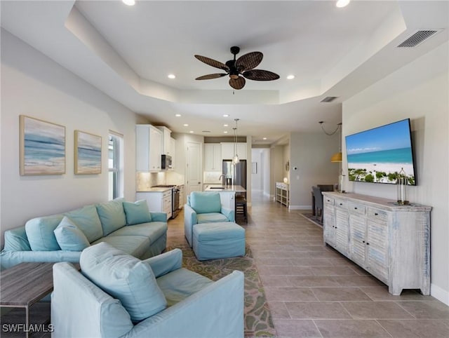 living room featuring sink, a raised ceiling, and ceiling fan