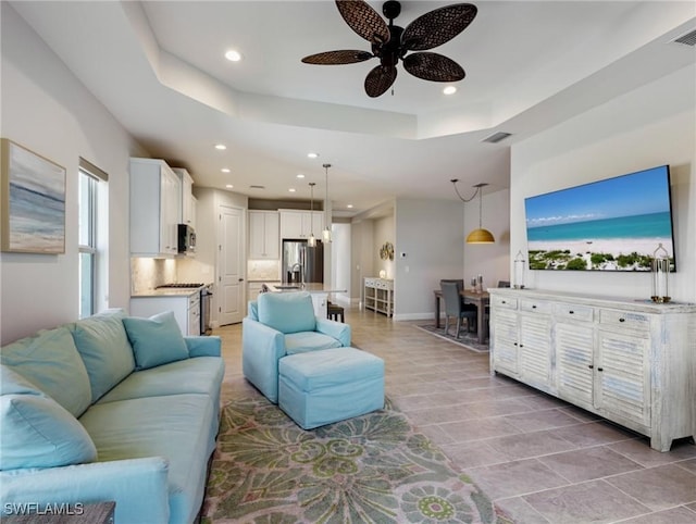 living room with a raised ceiling and ceiling fan