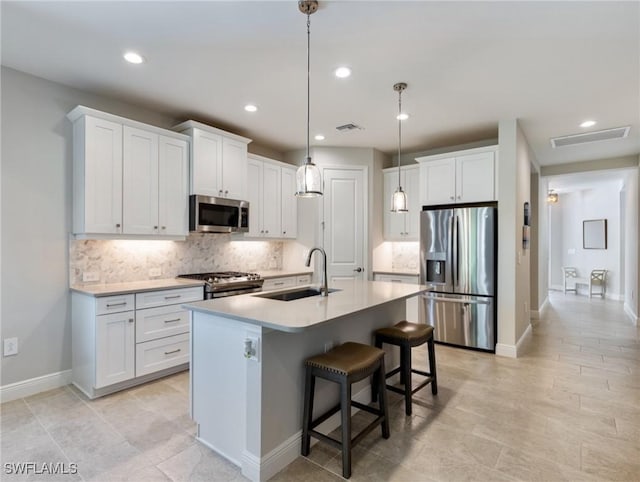 kitchen featuring sink, white cabinetry, decorative light fixtures, appliances with stainless steel finishes, and an island with sink