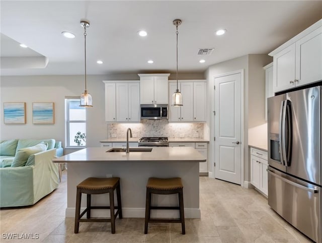 kitchen featuring pendant lighting, sink, appliances with stainless steel finishes, white cabinetry, and a kitchen island with sink