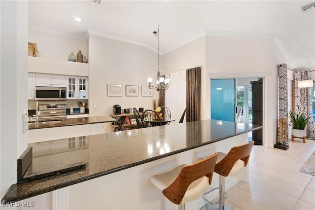 kitchen featuring a kitchen bar, hanging light fixtures, light tile patterned floors, appliances with stainless steel finishes, and white cabinets