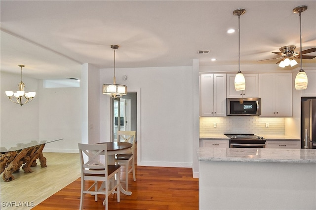 kitchen featuring white cabinetry, stainless steel appliances, decorative backsplash, dark wood-type flooring, and light stone countertops