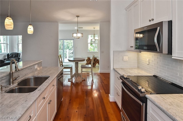 kitchen with white cabinets, appliances with stainless steel finishes, decorative light fixtures, sink, and light stone counters