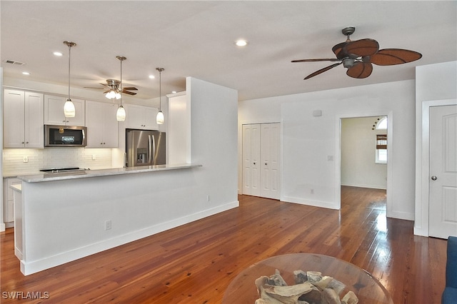 kitchen with dark hardwood / wood-style floors, decorative backsplash, white cabinetry, hanging light fixtures, and appliances with stainless steel finishes