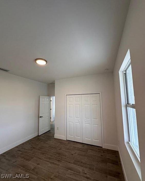 unfurnished bedroom with a closet, dark hardwood / wood-style flooring, and multiple windows