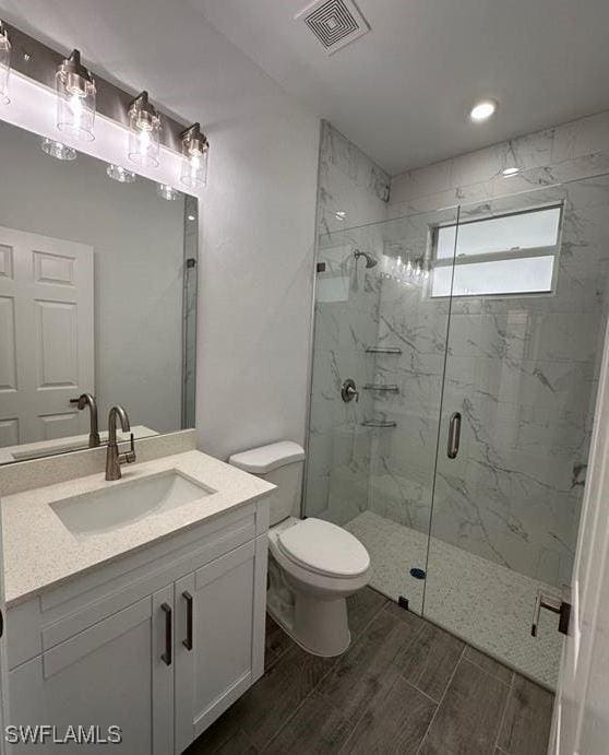 bathroom with a shower with shower door, vanity, and toilet