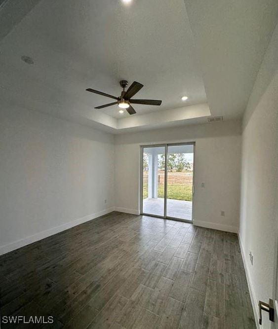 spare room with a raised ceiling, ceiling fan, and dark hardwood / wood-style flooring