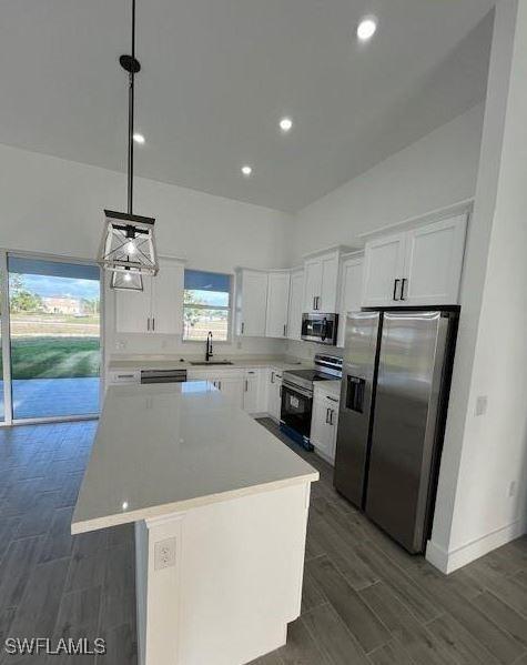 kitchen with a center island, appliances with stainless steel finishes, white cabinetry, and hanging light fixtures