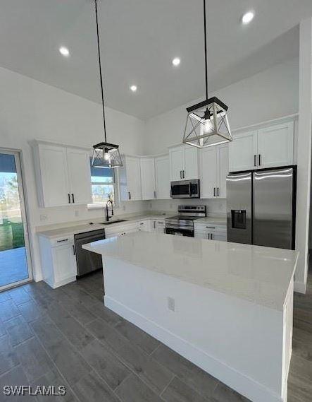 kitchen with white cabinetry, a center island, light stone countertops, pendant lighting, and appliances with stainless steel finishes