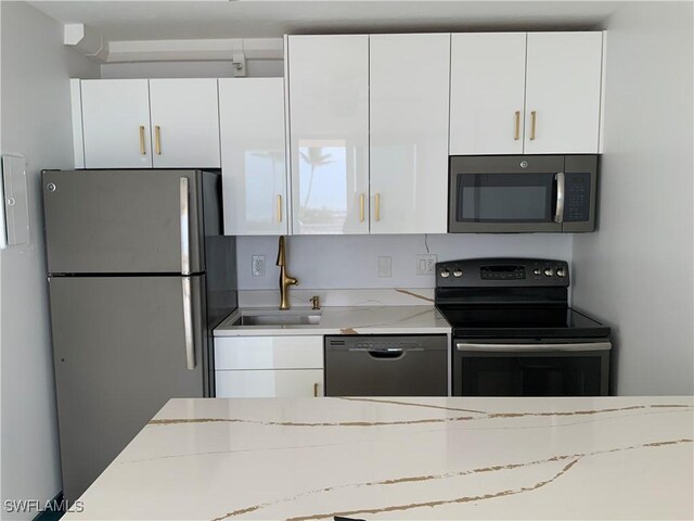 kitchen featuring sink, white cabinets, black appliances, and light stone counters