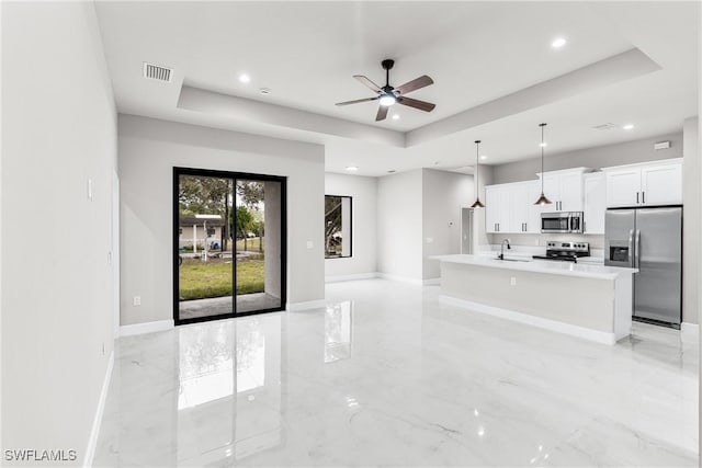 kitchen featuring a center island with sink, stainless steel appliances, pendant lighting, sink, and white cabinetry