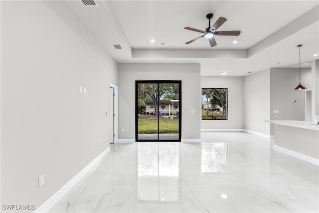 empty room with ceiling fan and a tray ceiling