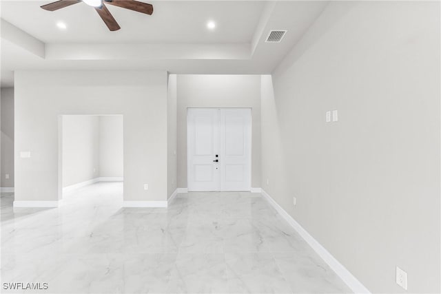 empty room with ceiling fan and a raised ceiling