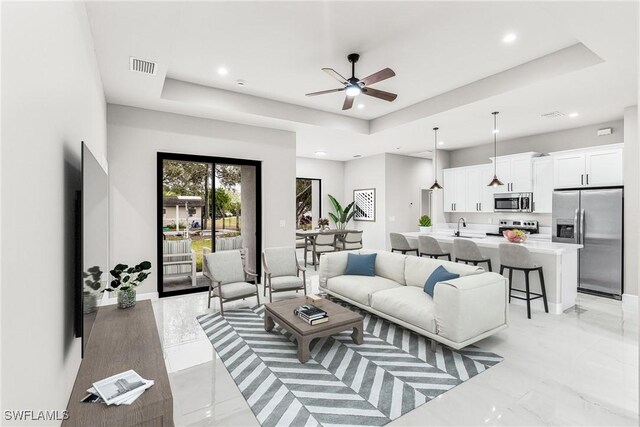 living room featuring sink, ceiling fan, and a tray ceiling