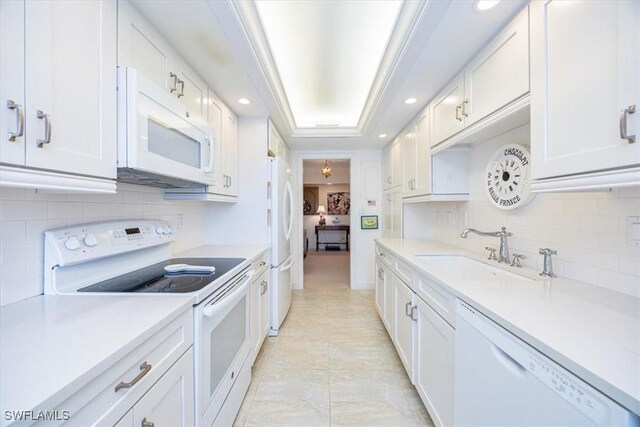 kitchen with sink, white appliances, white cabinetry, backsplash, and a tray ceiling