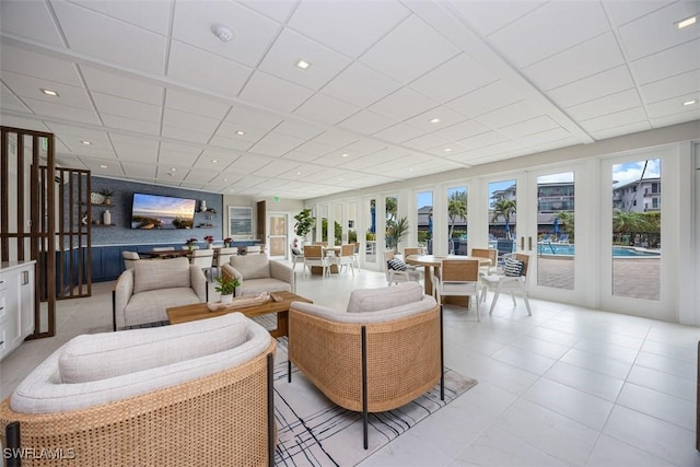 tiled living room with a drop ceiling and french doors