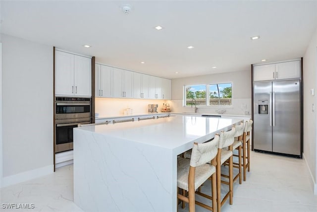 kitchen with appliances with stainless steel finishes, white cabinetry, backsplash, a kitchen breakfast bar, and a center island