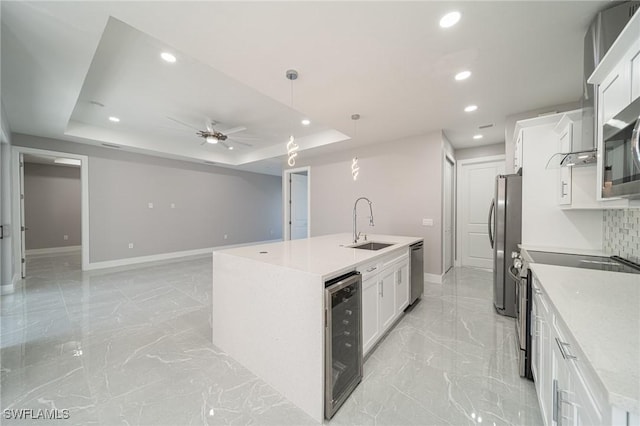 kitchen with white cabinets, wine cooler, a tray ceiling, stainless steel appliances, and a center island with sink