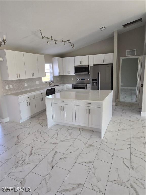 kitchen featuring stainless steel appliances, decorative backsplash, sink, white cabinetry, and lofted ceiling