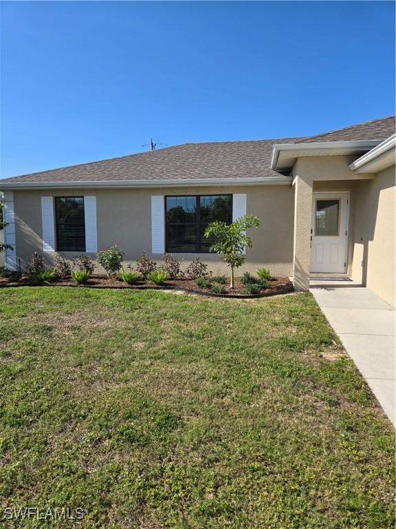 view of front of property with a shingled roof, a front yard, and stucco siding