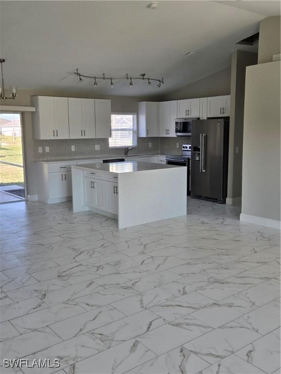 kitchen featuring vaulted ceiling, pendant lighting, a center island, stainless steel appliances, and white cabinetry