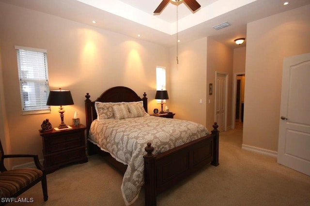 carpeted bedroom featuring multiple windows, ceiling fan, and a tray ceiling