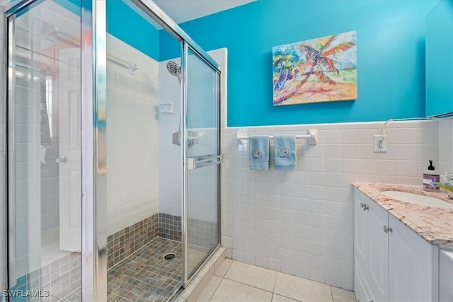 bathroom featuring tile patterned flooring, vanity, tile walls, and a shower with door