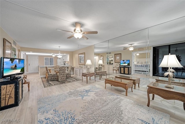 living room with a textured ceiling, light wood-type flooring, and ceiling fan with notable chandelier