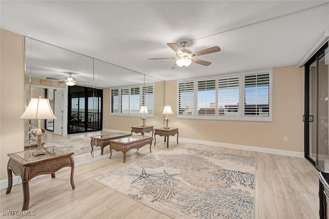 living area with ceiling fan, a textured ceiling, and light wood-type flooring