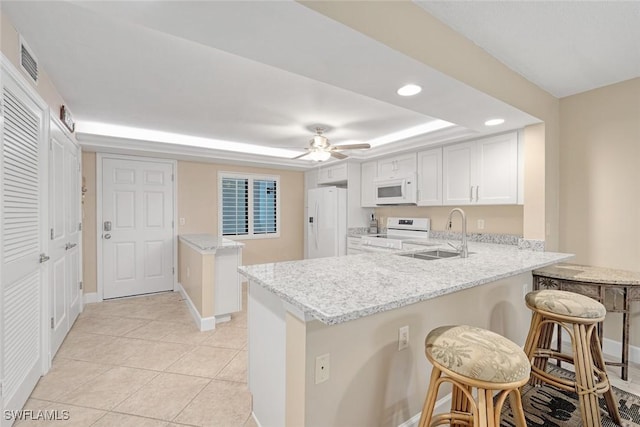 kitchen with kitchen peninsula, white cabinetry, light stone countertops, white appliances, and a kitchen bar