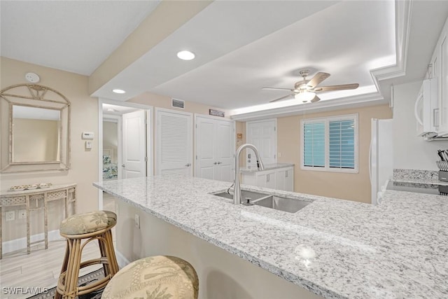 kitchen featuring sink, light wood-type flooring, light stone countertops, white appliances, and a breakfast bar