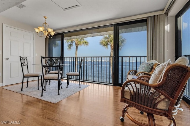 sitting room with an inviting chandelier, light wood-type flooring, expansive windows, and a water view