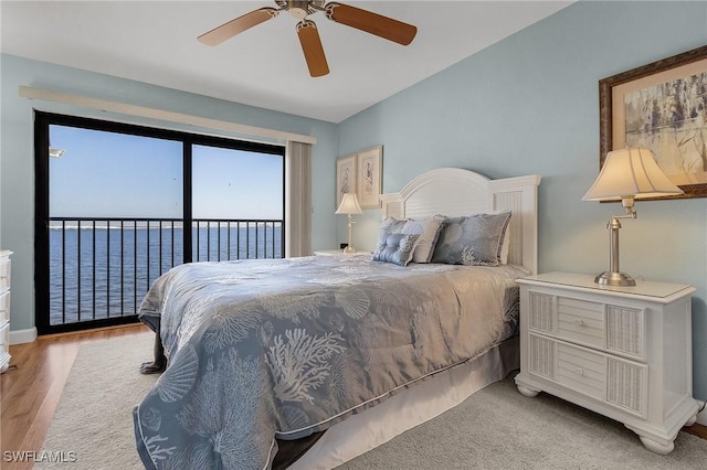 bedroom with access to exterior, ceiling fan, light hardwood / wood-style flooring, and a water view