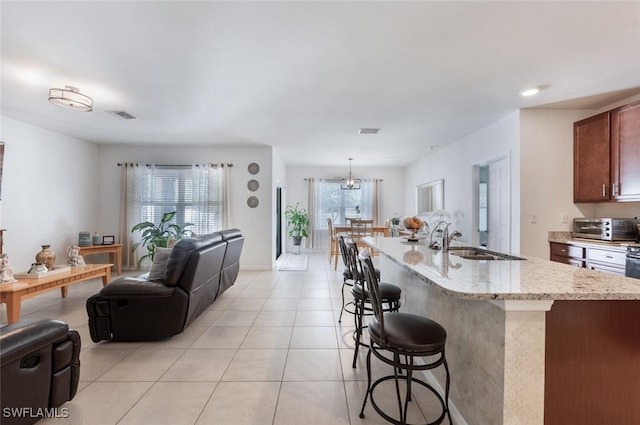 kitchen with sink, a center island with sink, hanging light fixtures, and light stone countertops