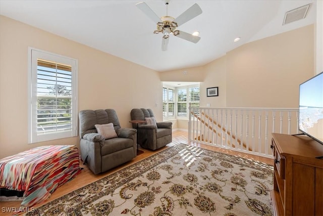 living area featuring lofted ceiling, wood-type flooring, ceiling fan, and a healthy amount of sunlight