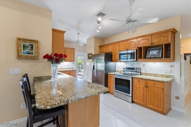 kitchen featuring kitchen peninsula, light stone countertops, stainless steel appliances, decorative backsplash, and a breakfast bar area