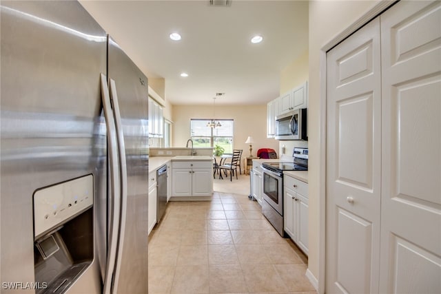 kitchen featuring light tile patterned floors, white cabinetry, appliances with stainless steel finishes, decorative light fixtures, and sink