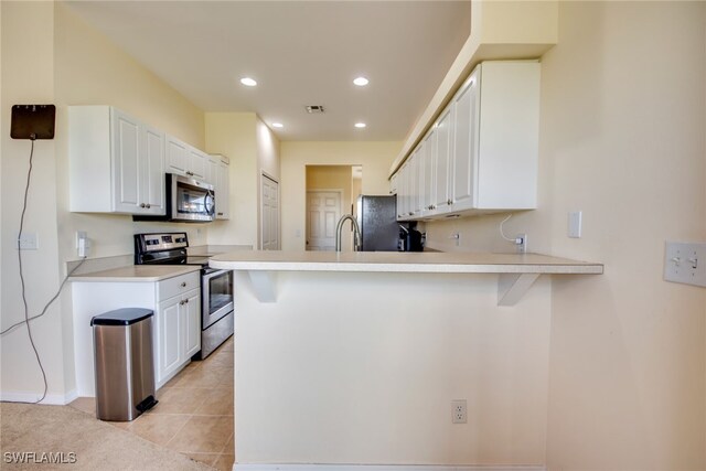 kitchen featuring light tile patterned floors, kitchen peninsula, stainless steel appliances, and white cabinetry