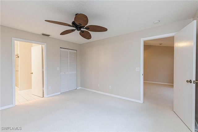 unfurnished bedroom featuring ensuite bathroom, light colored carpet, a textured ceiling, a closet, and ceiling fan